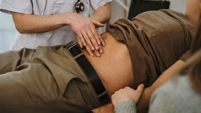 Gastroenterologe tastet den Bauch eines Mannes ab.